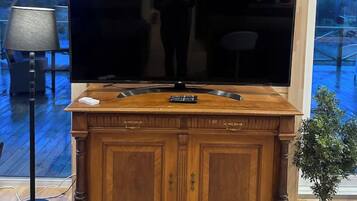 Een houten kast met een flatscreen televisie, een schilderij erboven en een plant in een pot ernaast.