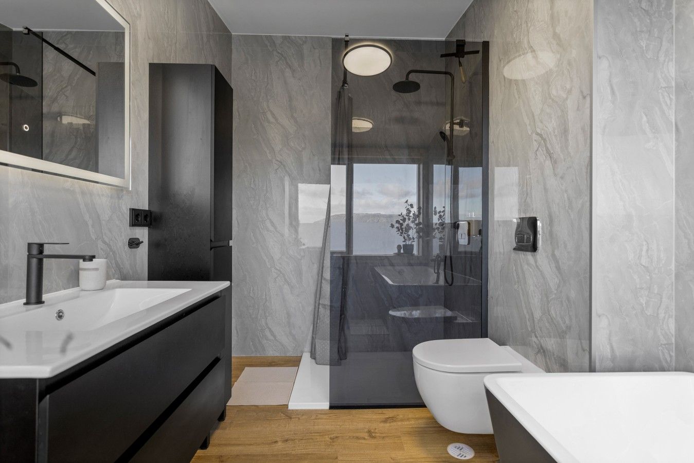 Et moderne badeværelse med et stort spejl, badekar, toilet og bruseområde.
