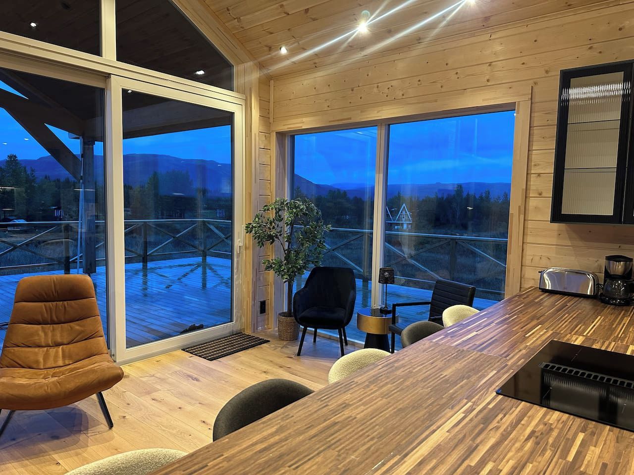 A modern kitchen with a wooden countertop, a dining area with chairs, and large windows offering a view of a snowy landscape.