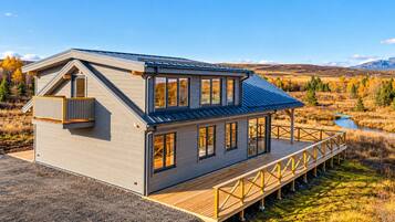 Eine zweistöckige Holzhütte mit einer Terrasse, umgeben von einer naturnahen Landschaft.