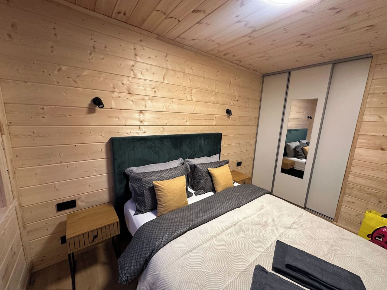 Ein Schlafzimmer mit Holzboden, einem Bett mit gemusterten Textilien, einem Kopfteil und einem Kleiderschrank mit Spiegel.