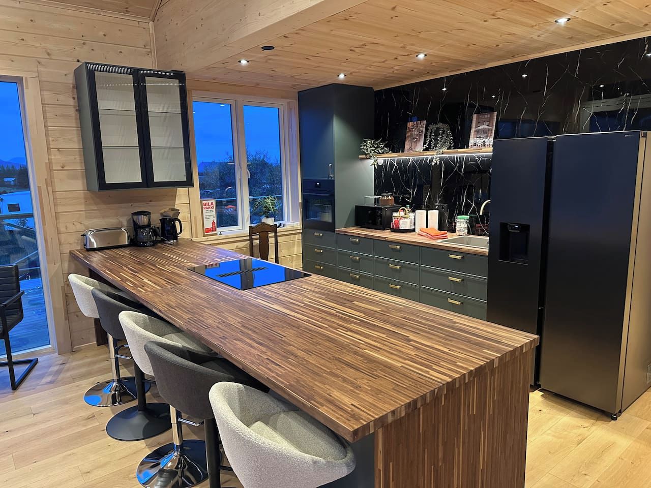 Een moderne keuken met een centraal eiland, barstoelen, een zwarte koelkast en uitzicht op de omgeving.