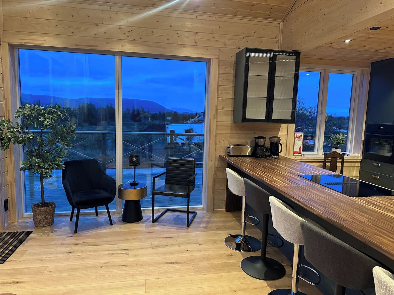 Une cuisine moderne avec un plan de travail en bois, des tabourets de bar et une grande fenêtre donnant sur un paysage pittoresque.