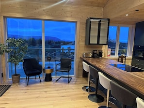 Eine moderne Küche mit einer Holzausziehtafel, Barhocker und einem großen Fenster mit Blick auf eine schöne Landschaft.