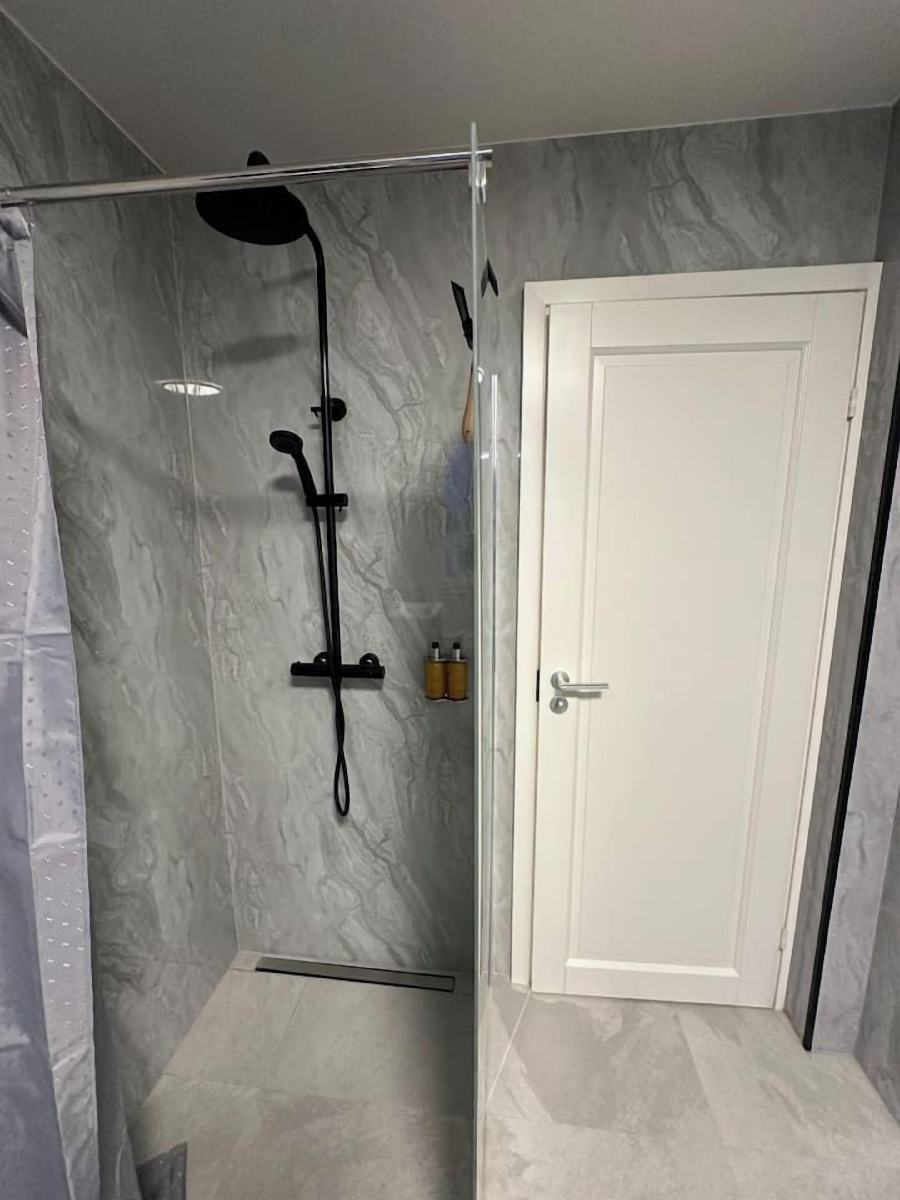 A shower with a glass door, a white door next to it, and a marble wall.
