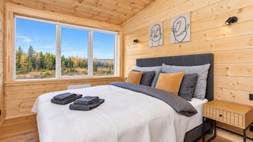 Une chambre avec un grand lit, des murs en bois, une fenêtre donnant sur les arbres et deux appliques murales.