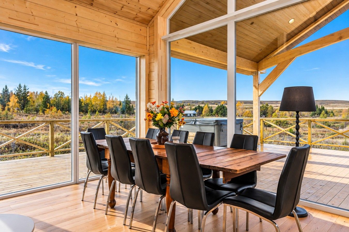 A wooden deck with a dining table and chairs, a flower vase, and a lamp.