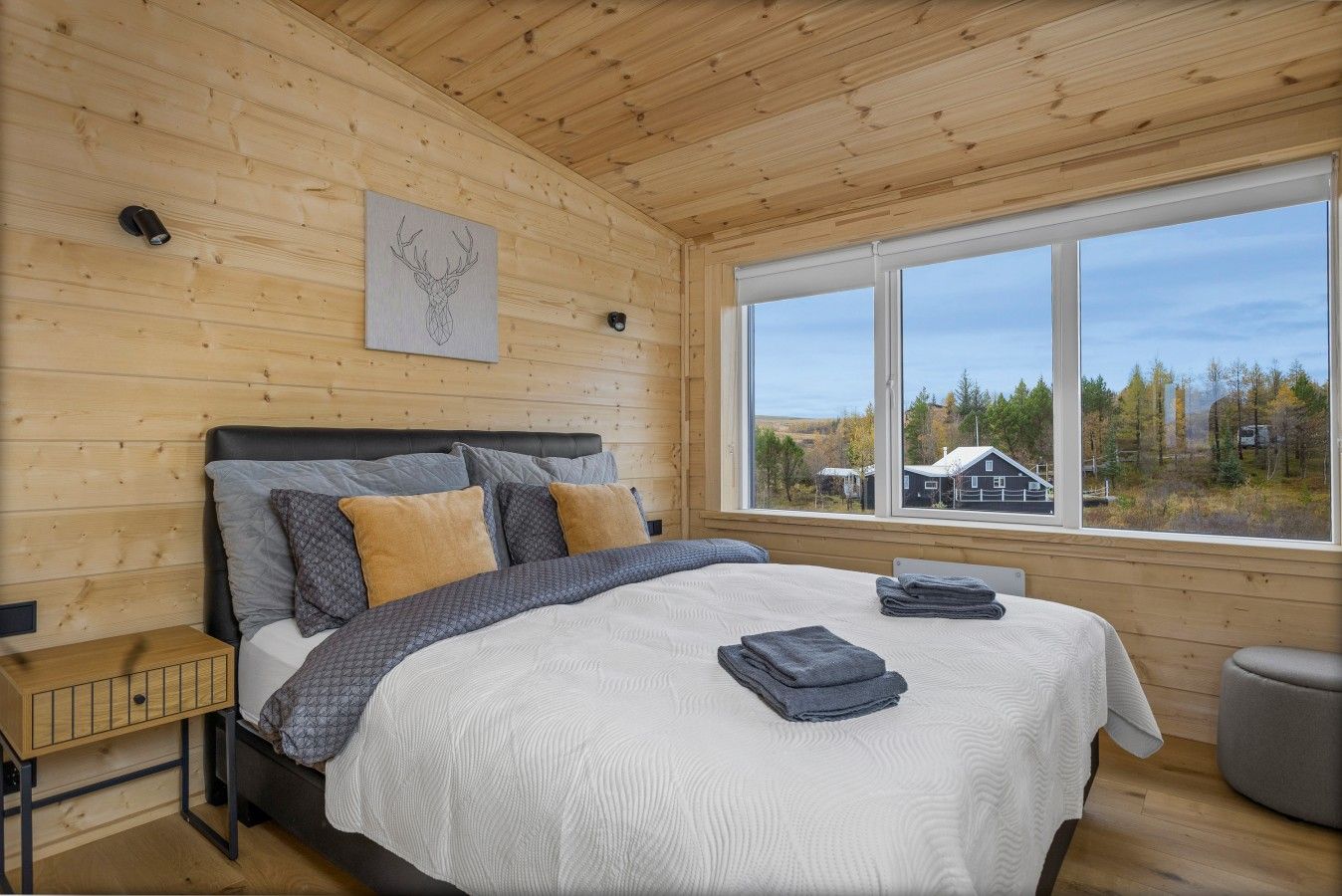 Ein Schlafzimmer mit einem großen Bett, Holzwänden, einem Fenster mit Aussicht und einem kleinen Nachttisch.