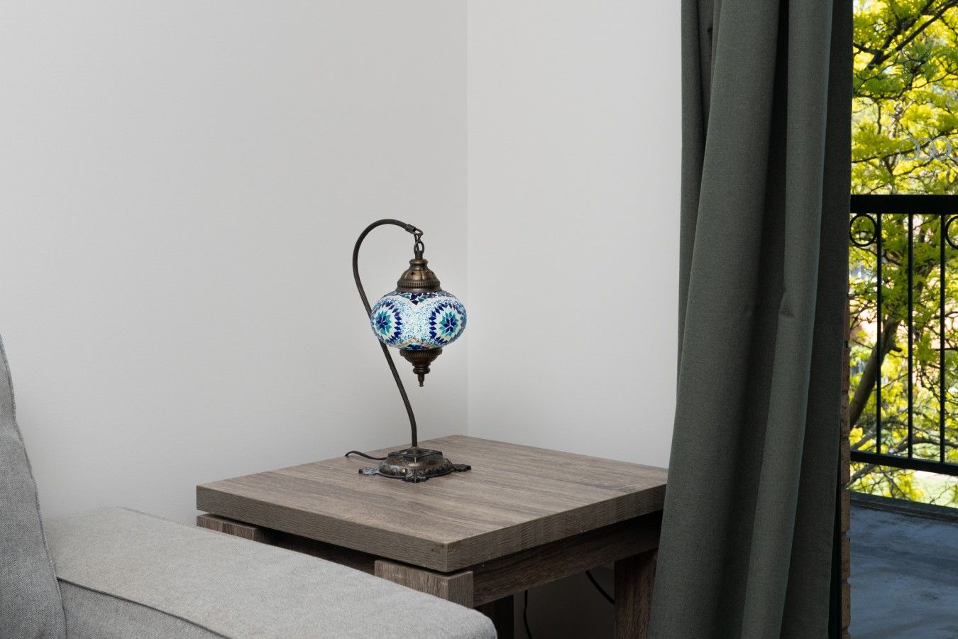 A corner of a room with a small table, a lamp, and a view of greenery outside.