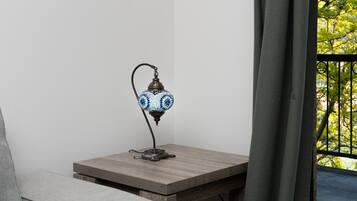 A corner of a room with a small table, a lamp, and a view of greenery outside.