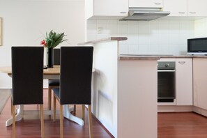 A modern kitchen with white cabinets, a built-in oven, and a dining area with two chairs. - 1BR with Pool and Large Balcony Near Manuka (Griffith)
