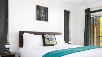 A hotel room with a large bed, a headboard, a nightstand with a lamp, a wall-mounted painting, and a window with curtains.