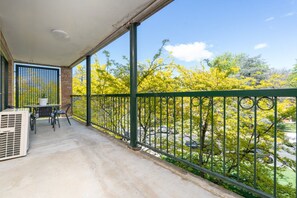 En balkon med bord og stole, en potteplante og udsigt til træer og en bil.