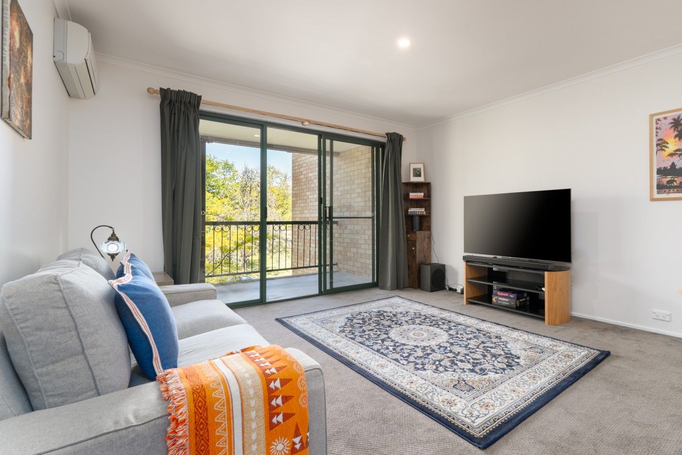 Ein Wohnzimmer mit einer Couch, einem Fernseher, einem gemusterten Teppich und einer Schiebetür, die auf einen Balkon führt.