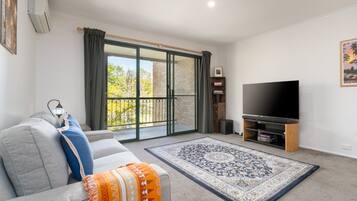 A living room with a sofa, a television, a patterned rug, and a sliding glass door leading to a balcony.