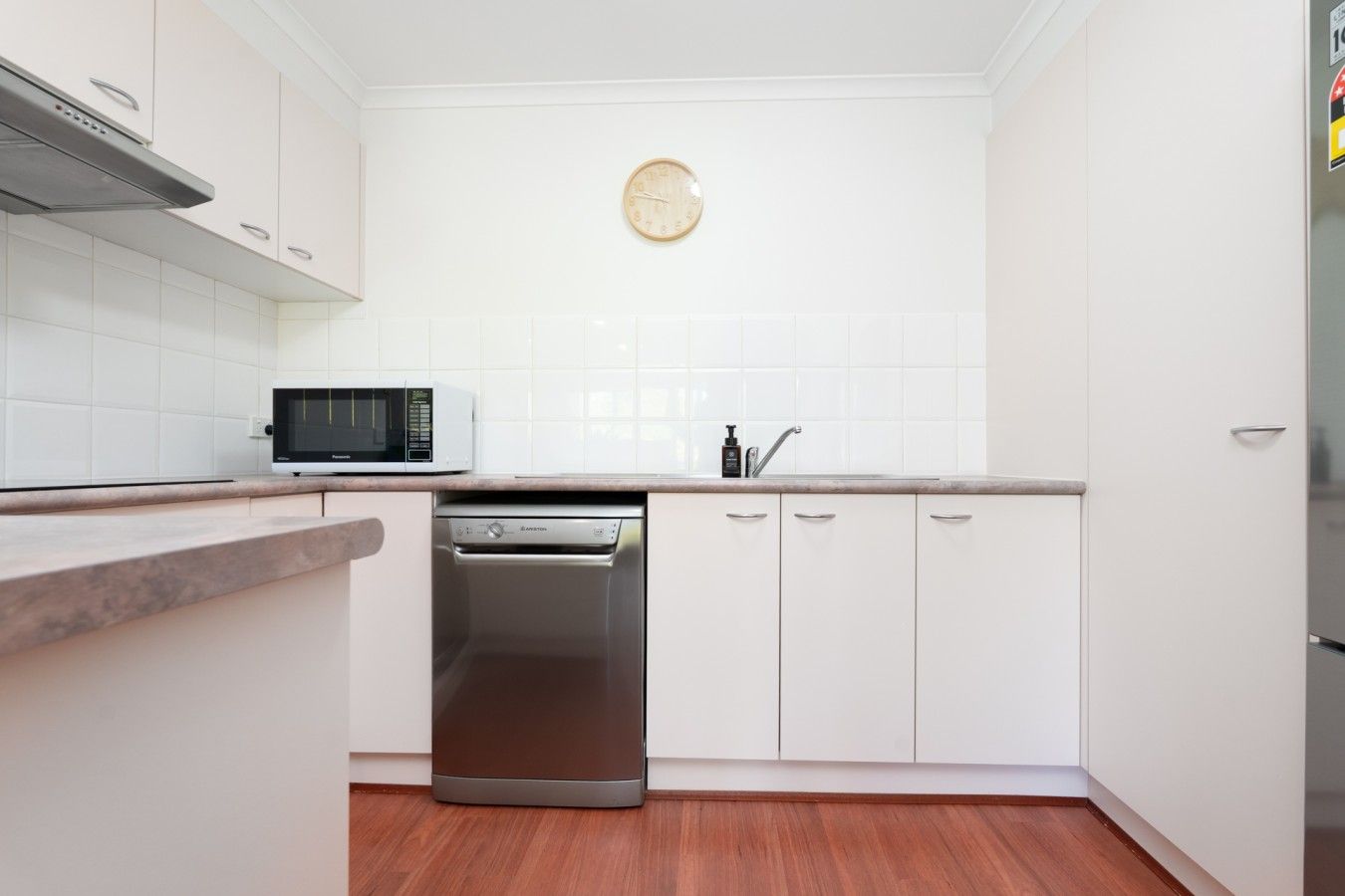 A kitchen with white cabinets, a microwave, a dishwasher, and a clock on the wall.