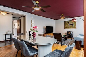 A modern living room with a round glass table, comfortable seating, a flat-screen TV, and a ceiling fan. - 7BR | 2 Modern Apartments Near Reforma | Sleeps 14 (Mexico City)