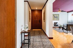 A hallway with a wooden door, a small table with a potted plant, and a living area with a sofa and a coffee table. - 7BR | 2 Modern Apartments Near Reforma | Sleeps 14 (Mexico City)