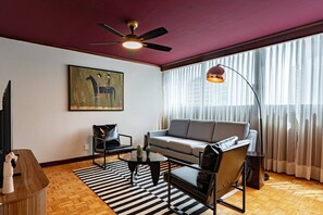 A living room with a sofa, armchairs, a coffee table, a painting, and a ceiling fan. - 7BR | 2 Modern Apartments Near Reforma | Sleeps 14 (Mexico City)