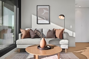 A modern living room with a grey sofa, a round wooden coffee table, and a framed artwork on the wall. - High-Rise 2-Bed Apartment Near Southbank (South Melbourne)
