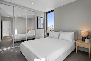 A modern hotel room with a large bed, a city view, a sliding door, and a bedside table with a lamp. - High-Rise 2-Bed Apartment Near Southbank (South Melbourne)