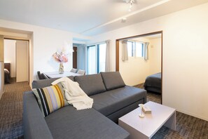 Ein modernes Wohnzimmer mit einem grauen Sofa, einem weißen Couchtisch und einem Essbereich im Hintergrund.