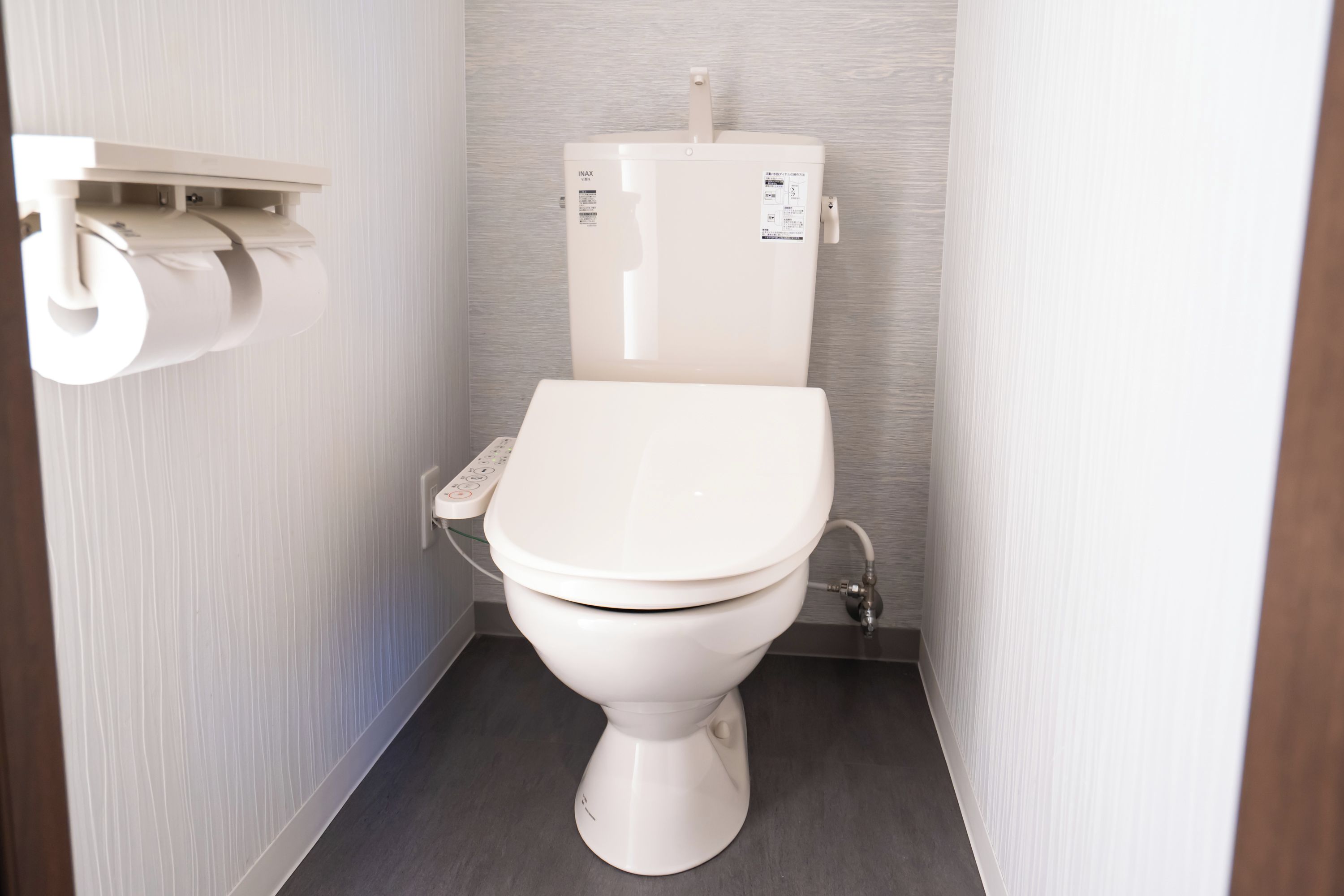 A modern toilet with a control panel, a toilet paper holder, and a visible water pipe.