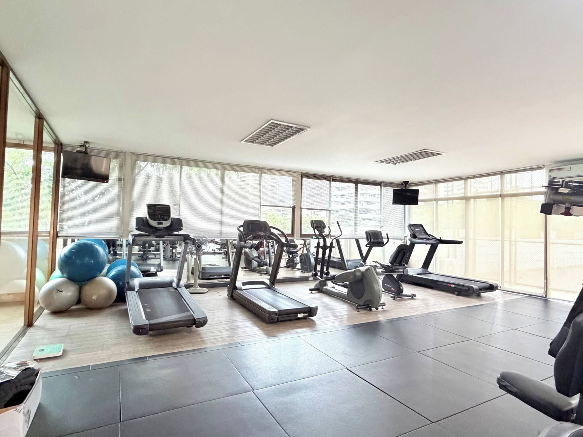 A gym with various exercise equipment, large windows, and a tiled floor.