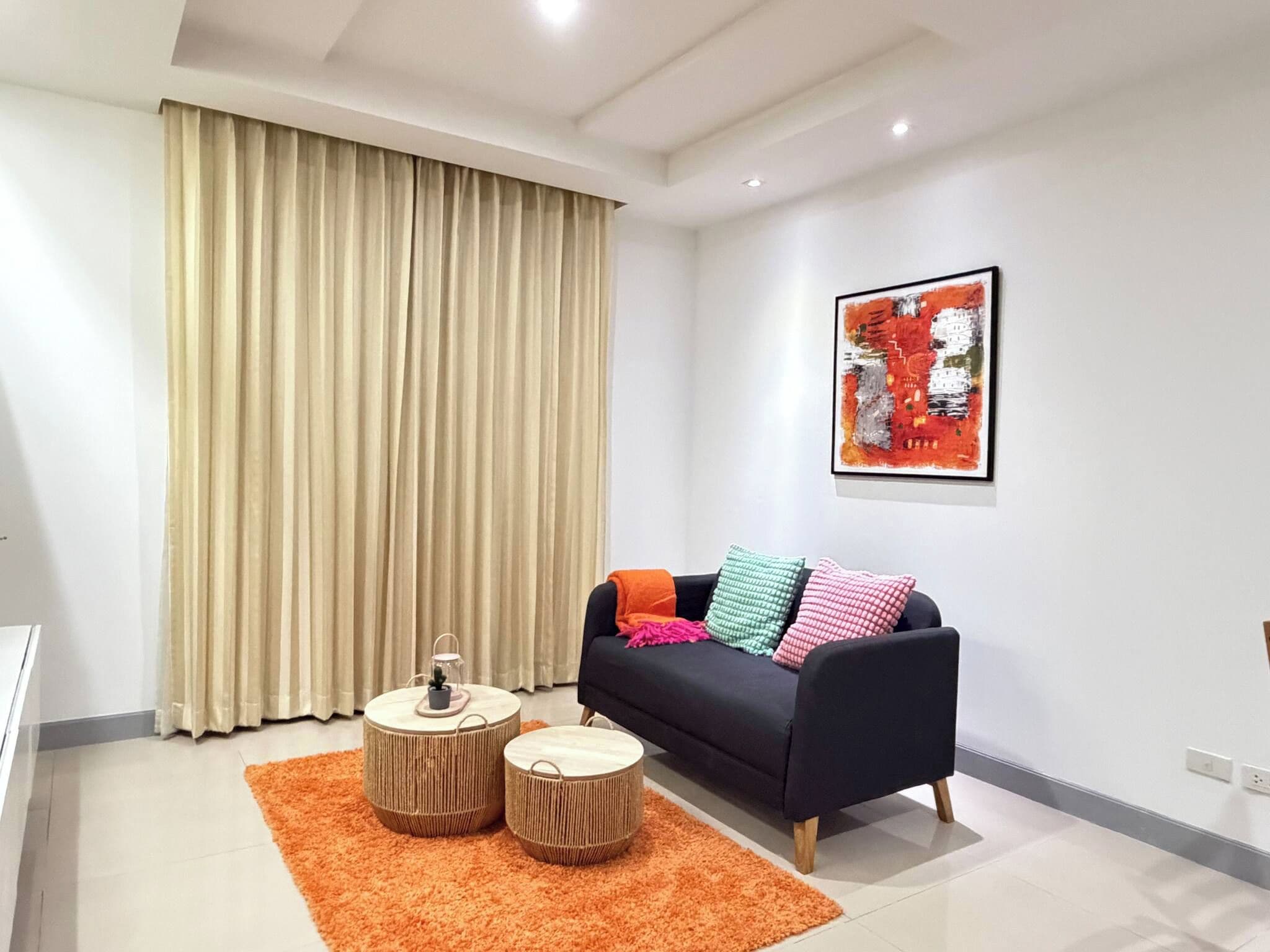 A modern living room with a sofa, two round wooden side tables, a colorful rug, and a large abstract painting on the wall.