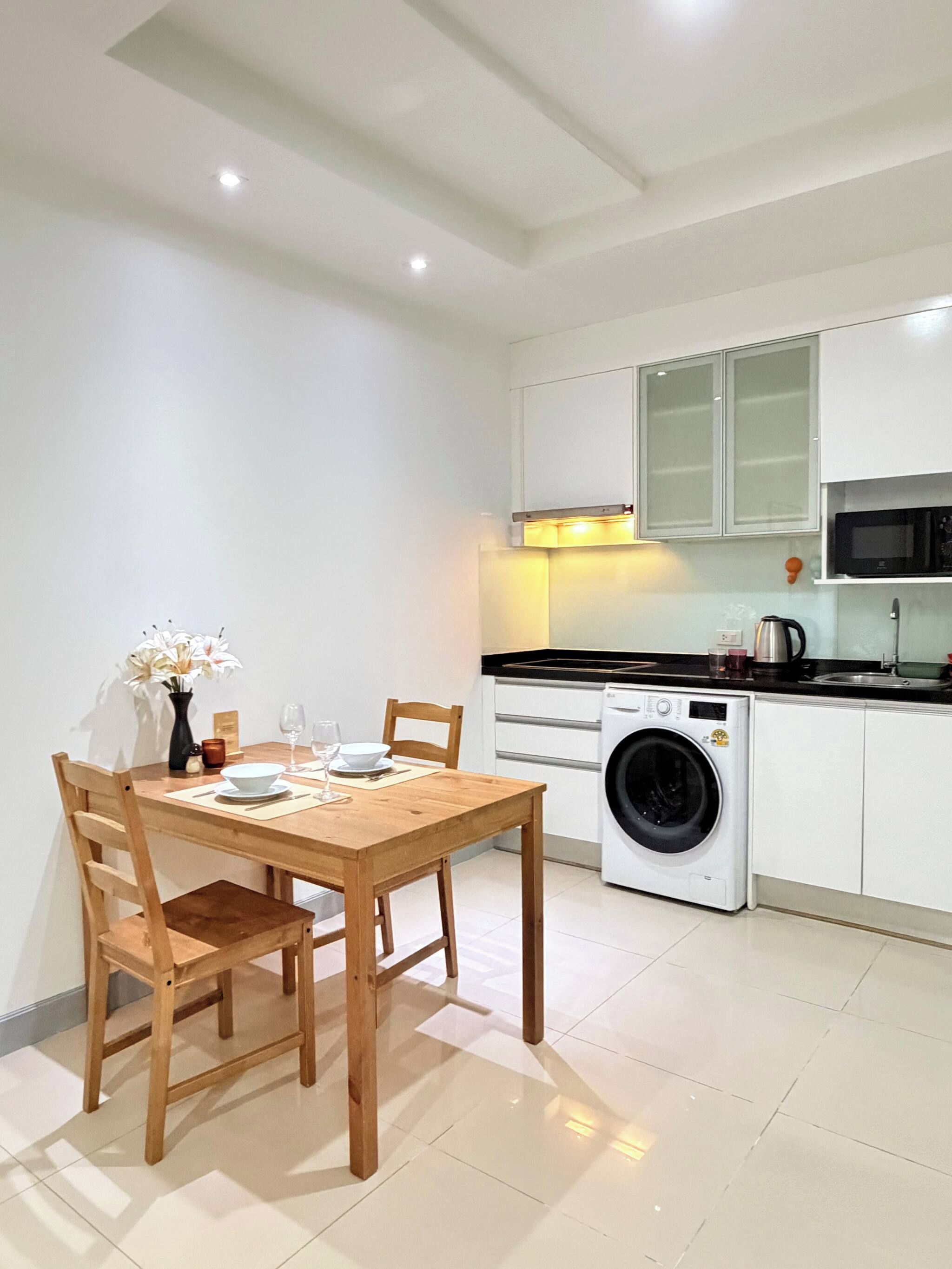 A compact kitchen with a washing machine, a microwave, and a dining area with a table and chairs.