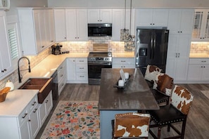 A modern kitchen with white cabinets, stainless steel appliances, and a central island with seating. - The Inn on Turville Creek + 6 Waterfront Cottages (Berlin)