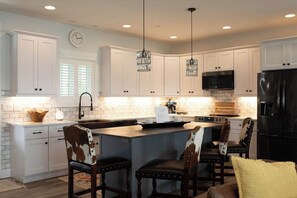A modern kitchen with white cabinetry, a central island, and pendant lighting. - The Inn on Turville Creek + 6 Waterfront Cottages (Berlin)