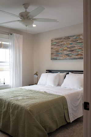 A bedroom with a bed, a ceiling fan, a painting, and a window with curtains. - The Inn on Turville Creek + 6 Waterfront Cottages (Berlin)