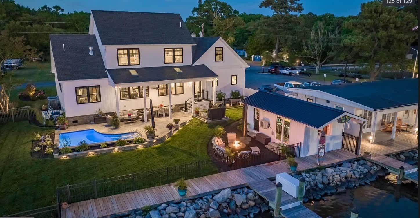A two-story house with a swimming pool, outdoor seating area, and a dock.