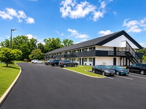 Een motel met twee verdiepingen, een parkeerplaats, een overdekte gang en een heldere lucht.