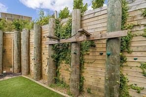 A wooden climbing wall with colorful holds and a grassy area in front. - Kuaotunu Heights | Epic Ocean Views & Outdoor Living (Kūaotunu)