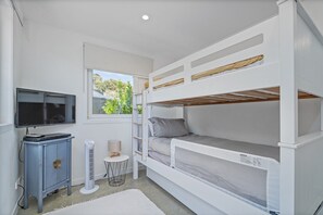Ein Stockbett mit Fernseher und einem kleinen Tisch, ein Fenster mit Blick auf Grünflächen und eine weiße Wand.