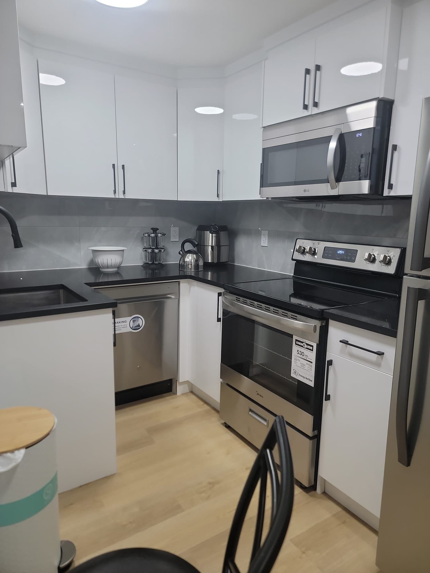 A modern kitchen with white cabinets, a stainless steel microwave, an oven, and a dishwasher.