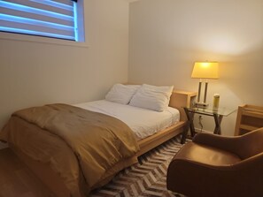 Una habitación de hotel con una cama, una mesita de noche con lámpara, una silla y una alfombra estampada.