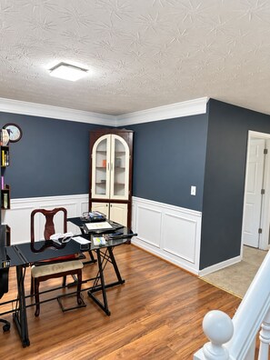 A room with a wooden floor, a desk with a chair, a cabinet, and a clock on the wall. - Adorable 4-bedroom house with AC in welcoming Covington (Covington)