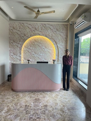 A reception desk with a marble wall backdrop, a ceiling fan, and an air conditioning unit. - Shivpalace Hotel  (Jaipur)