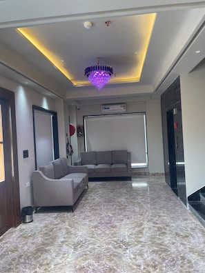 A modern living room with a marble floor, a sofa, a chandelier, and a large window. - Shivpalace Hotel  (Jaipur)