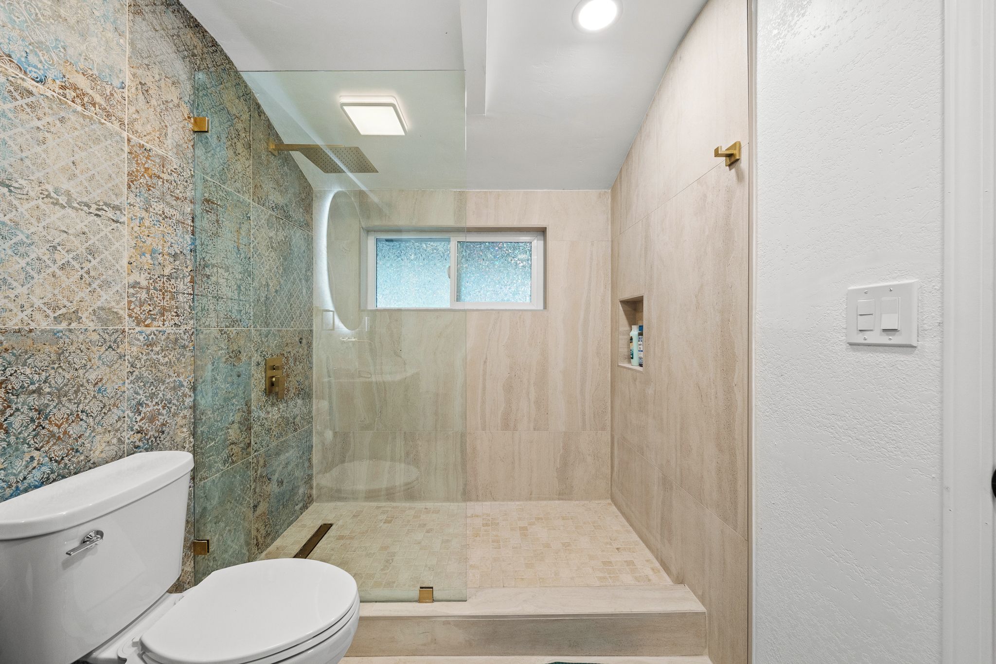 A bathroom with a shower, toilet, and a window.