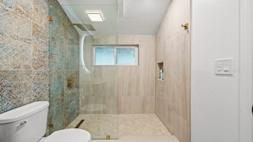 A bathroom with a shower, toilet, and a window.