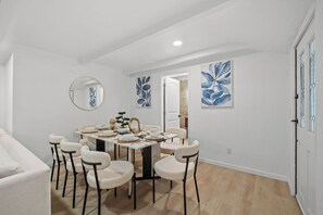 A dining area with a round table set for six, surrounded by six chairs, a round mirror, and two wall-mounted floral paintings. - Entire Private Home with 3 Beds, Pool, Sauna, Gym, Parking Yard, Ranch Style (Spring Valley)
