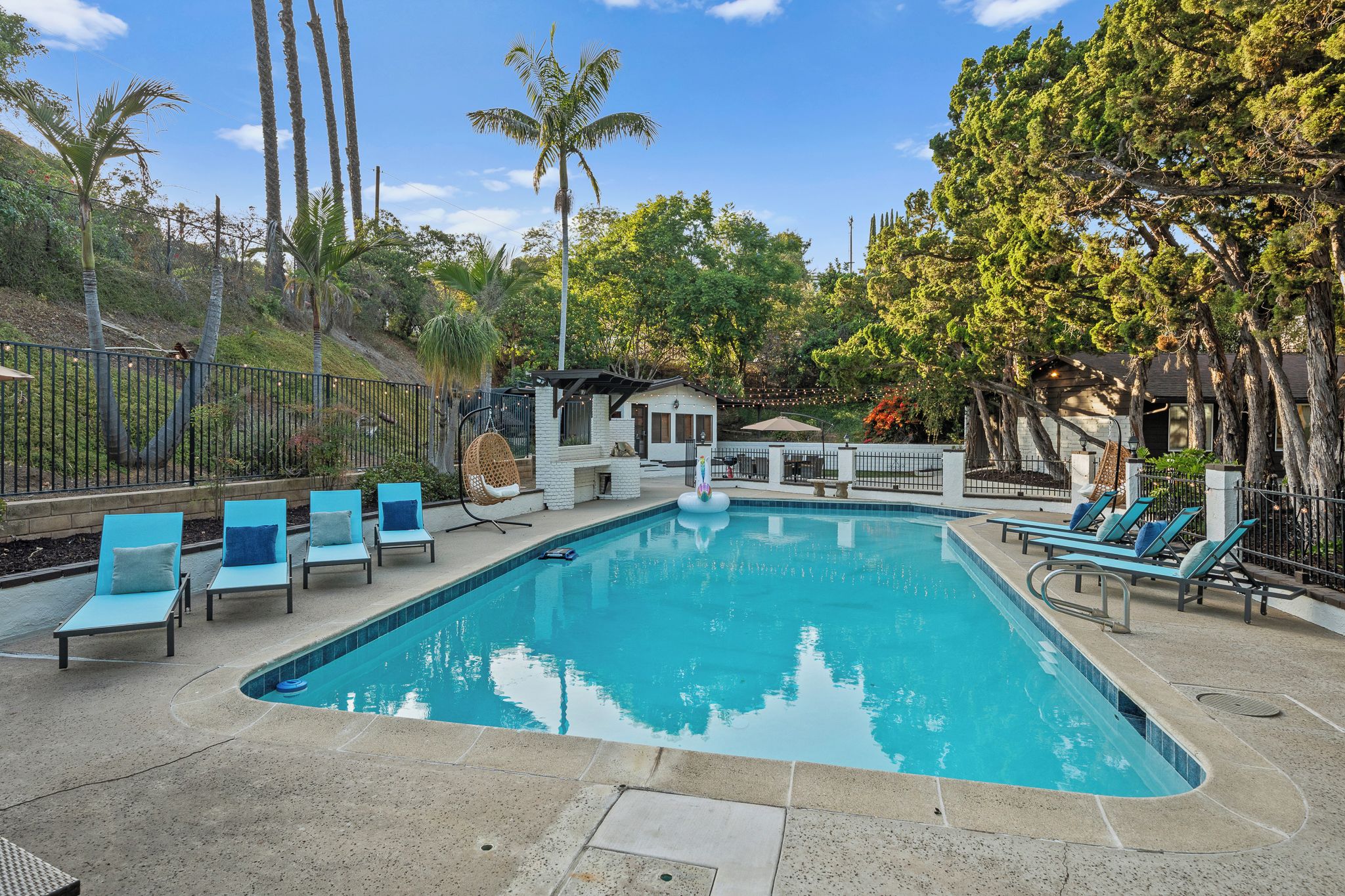 A swimming pool with lounge chairs, a small building, and surrounding trees.