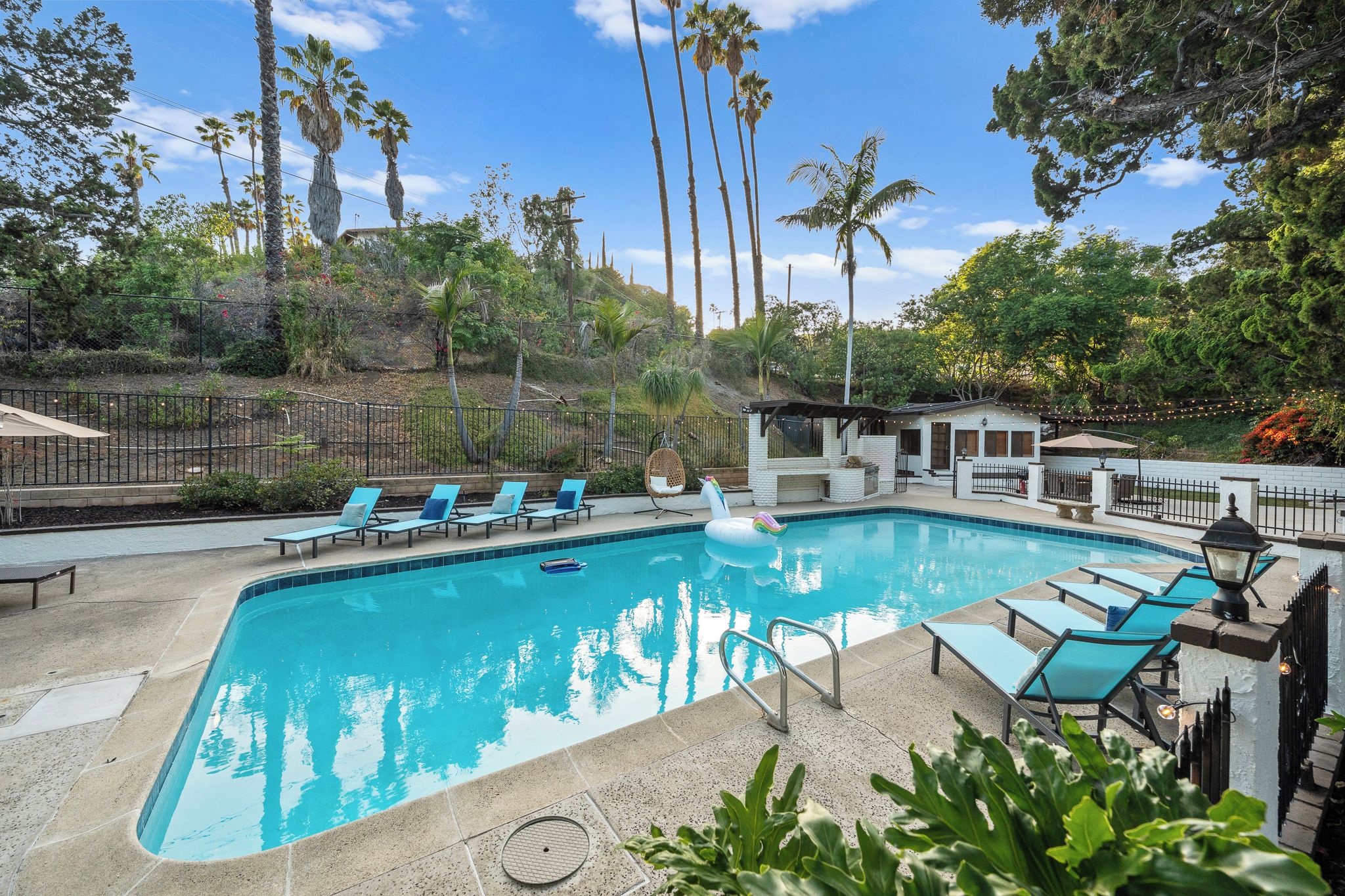 A swimming pool with lounge chairs, a small pavilion, and tall palm trees in the background.