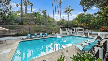 A swimming pool with lounge chairs, a small pavilion, and tall palm trees in the background.