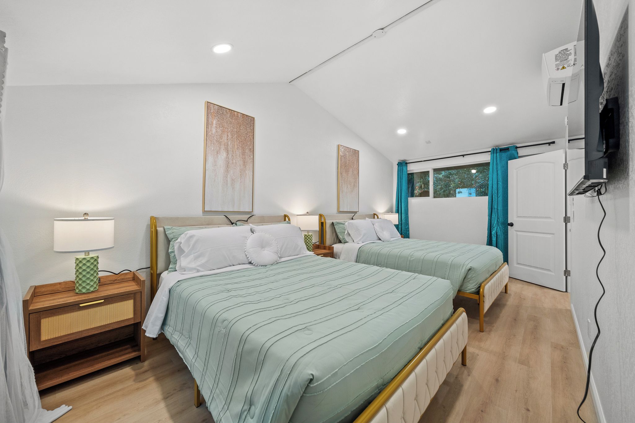 Une chambre avec deux lits, une table de chevet, une lampe et une fenêtre avec des rideaux.