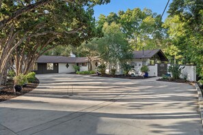 A residential area with a paved driveway, a house with a stone facade, and surrounding greenery.